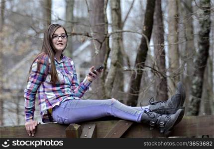 A beautiful teen girl sitting outdoors with her cell phone.