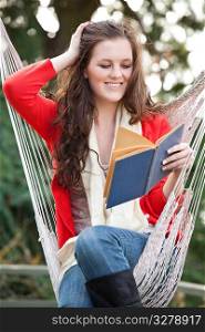 A beautiful teenager sitting on a hammock reading a book