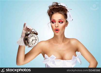 A beautiful vintage pin-up girl in a white wedding dress being late in the morning and holding a retro alarm clock in her hand.