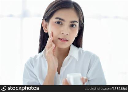 A beautiful woman asian using a skin care product, moisturizer or lotion taking care of her dry complexion. Moisturizing cream in female hands .