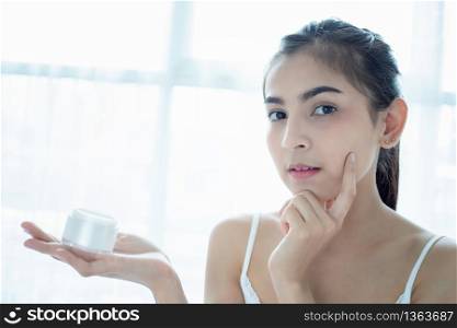 A beautiful woman asian using a skin care product, moisturizer or lotion taking care of her dry complexion. Moisturizing cream in female hands .