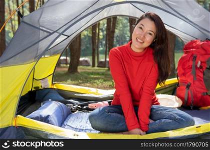 A beautiful woman in a red shirt camping, sitting in a yellow tent with red backpack In the middle of a pine beautiful forest beside a lake, Pang Oung, Mae Hong Son, Thailand.. Women camping tent.