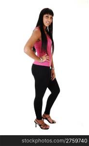 A beautiful woman in black tights and a pink top standing in profile and smiling and her long black hair hanging down, over white background.