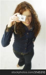 A beautiful woman poses with a digital camera taking a photo.