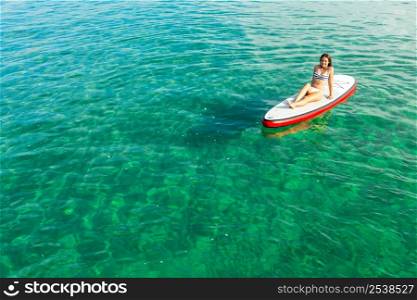 A beautiful woman sitting over a paddle surfboard and relaxing on a beautiful sunny day