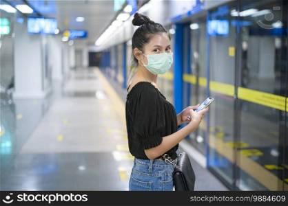 A beautiful woman wearing a surgical mask using phone while waiting a train in metro, technology and covid19 concept. Beautiful woman wearing a surgical mask using phone while waiting a train in metro, technology and covid19 concept