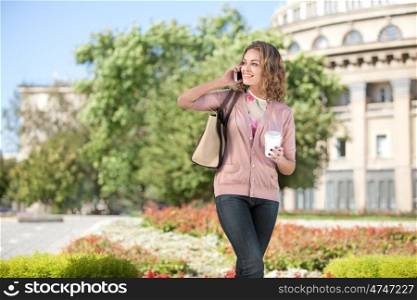 A beautiful woman with the phone holding a cup of take away coffee in a summer city.