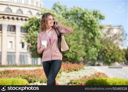 A beautiful woman with the phone holding a cup of take away coffee in a summer city.