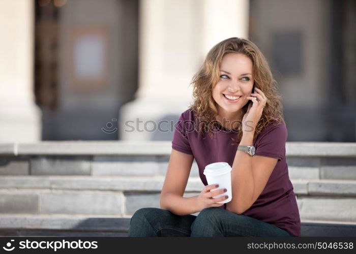 A beautiful woman with the phone holding a cup of take away coffee.