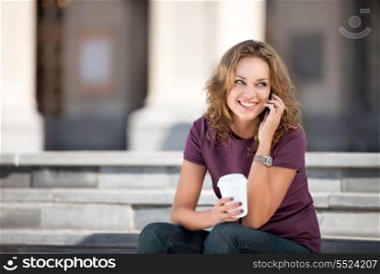 A beautiful woman with the phone holding a cup of take away coffee.