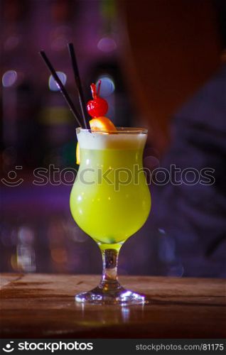 A beautiful yellow cocktail with white foam and orange slice and cherry in a tall glass. close-up