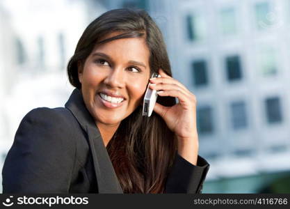 A beautiful young Asian businesswoman with a wonderful smile chatting on her cell phone with an out of modern city behind her.