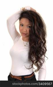 A beautiful young Asian woman standing in the studio holding one handon her head, with her long curly brunette hair, for white background.
