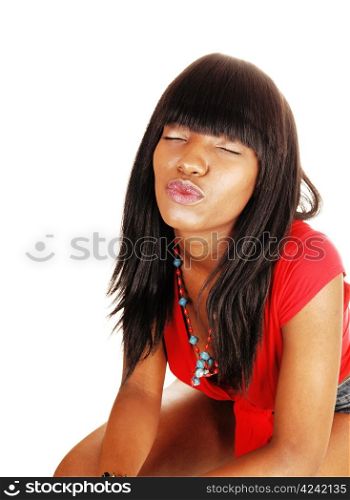 A beautiful young black woman in a red blouse and long black hairsitting for white background and giving a kiss with closed eyes.