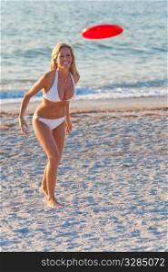 A beautiful young blond woman in a white bikini playing frisbee at the beach