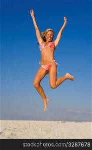 A beautiful young blond woman jumps high on a sandy beach