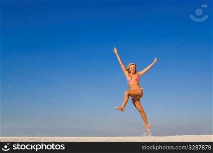 A beautiful young blond woman jumps high on a sandy beach