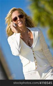 A beautiful young blond woman on the phone in a sunny location backed by palm tree