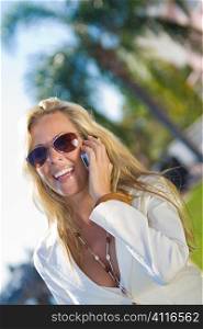 A beautiful young blond woman on the phone in a sunny location backed by palm trees