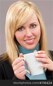 a beautiful young blond woman smartly dressed and drinking a mug of tea or coffee