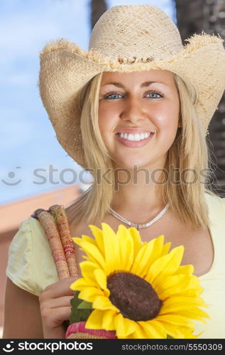 A beautiful young blond woman wearing a straw cowboy hat and smiling while carrying a shopping bag of sunflowers