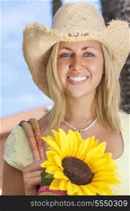 A beautiful young blond woman wearing a straw cowboy hat and smiling while carrying a shopping bag of sunflowers