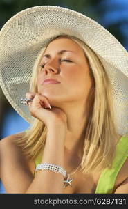 A beautiful young blond woman wearing a sun hat eyes closed enjoyed getting a sun tan on her face