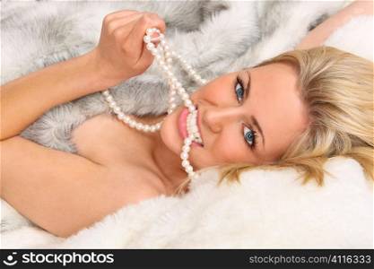 A beautiful young blond woman wrappeded in (fake) fur and biting a pearl necklace