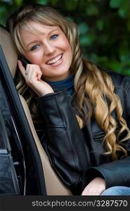 A beautiful young blonde woman sitting in her car and talking on her mobile phone