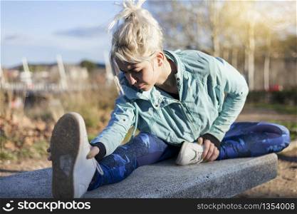 A beautiful young blonde woman sitting in the grass and stretching in a park