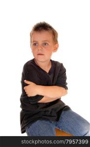 A beautiful young boy sitting on a chair in a black t-shirt, hugginghimself, isolated for white background.