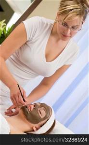 A beautiful young brunette woman having a chocolate face mask applied by a beautician