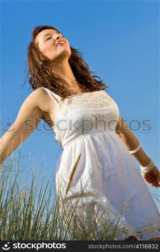 A beautiful young brunette woman walking through tall grass illuminated by natural late evening golden sunshine and looking ecstatic