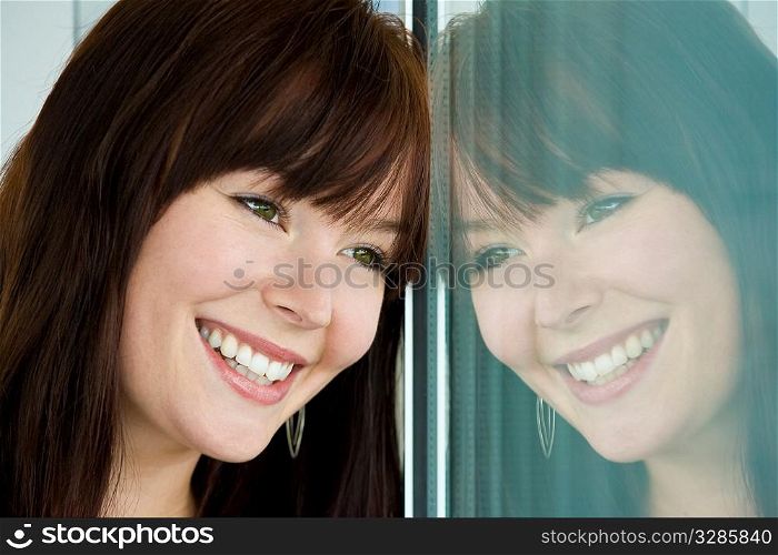 A beautiful young brunette woman with green eyes and a lovely laugh looks at her reflection in a window