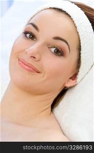 A beautiful young brunette woman with striking brown eyes and a friendly smile relaxes at a health spa after a facial treatment and make up