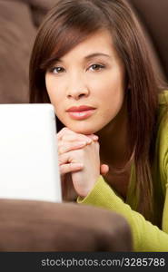 A beautiful young chinese asian oriental woman laying down using a white laptop on her sofa or settee