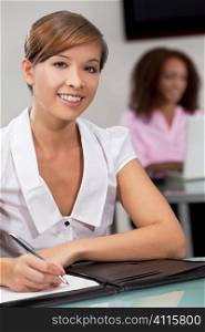 A beautiful young Chinese oriental Asian woman working in an office with her African American colleague out of focus behind her.