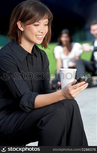 A beautiful young Eurasian woman with a wonderful smile texting on her cell phone while drinking coffee