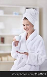 A beautiful young girl in a bathrobe and a towel with a cup of coffee