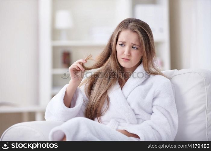 A beautiful young girl in a bathrobe looking at the tips of his hair