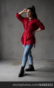 a beautiful young girl in a red shirt with a necklace with a handmade ornament on her neck is posing in a photo studio