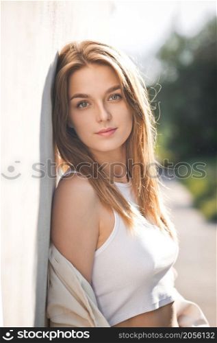 A beautiful young girl is leaning against the wall in the sunlight.. A beautiful portrait of a young girl in the sunlight 3680.