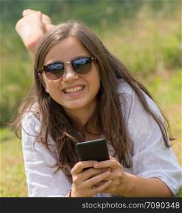 a beautiful young girl with sunglasses is using the smartphone