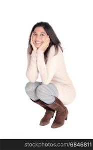 A beautiful young Hispanic woman in a knitted dress and brown bootscrouching on floor, the face in her hands, isolated on white background.. Happy woman crouching on floor.