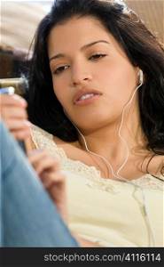 A beautiful young Hispanic woman laying down and enjoying a mussic on her mp3 player