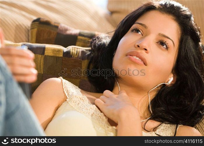 A beautiful young Hispanic woman laying on a settee and listening to music on her mp3 player