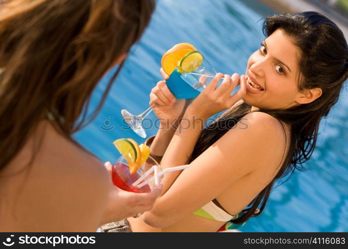 A beautiful young Hispanic woman sitting by a swimming pool and enjoying a cocktail with her friends