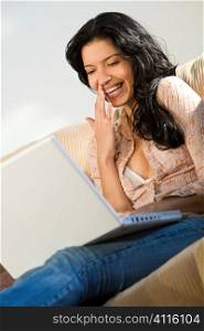 A beautiful young Hispanic woman using her laptop and laughing