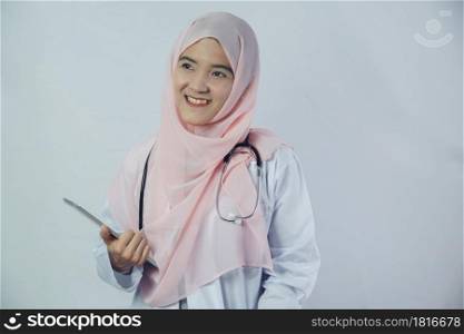 A beautiful young Islamic doctor woman in hijab dress with stethoscope and using tablet standing on white background