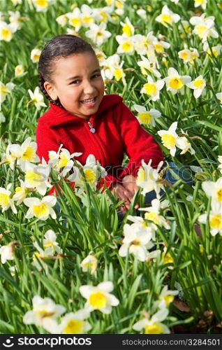 A beautiful young mixed race girl sitting and laughing in a field of daffodils